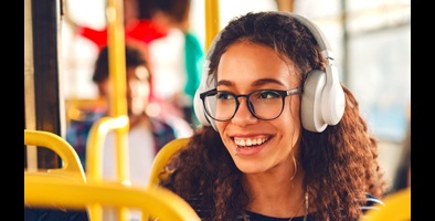 Young woman wearing headphones, sitting on bus and smiling at someone off-camera. 
