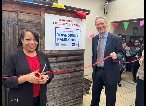 Brenda Dacres, the Mayor of Lewisham, and Councillor Chris Barnham cut a ribbon to officially open the new Family Hub. They are standing outside a building, poised and ready to cut the ribbon. 