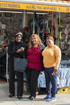 Cllr Powell is standing in between two Black female shop owners