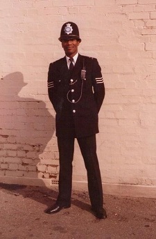 An old picture shot against a brick wall, probably from the 1970s, of Dr David Michael MBE wearing his police uniform