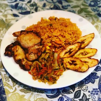 Fried chicken served with plantain, jollof rice and onions and peppers