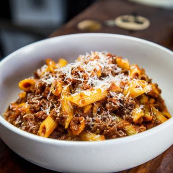 A white bowl full of penne and beef ragu with freshy grated parmesan on top