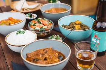 A selection of earthenware bowls on a wooden table containing rice, chutneys and a variety of Pakistani dishes