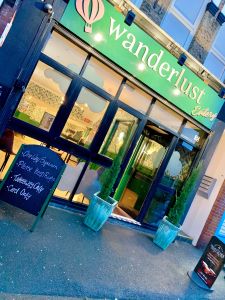 A view of Wanderlust cafe from the pavement, the signage is yellow on a green background