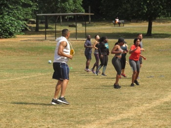 A group of males and females exercising outdoors at a social distance