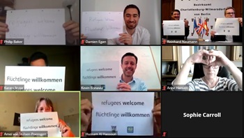 Philip Baker, Damien Egan, Reinhard Naumann, Karam Lessa, Kevin Bonavia, Anne Handen, Amel VonHulsen-Peonsgen and Hussam Al Sassoun hold up signs saying 'refugees welcome' on a video call