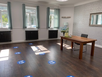 Room with a desk, chair, three large windows and social distancing stickers on the floor.