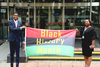 Lewisham Young Mayor, Femi Komolafe, and Angella Billy holding a large Black History Month flag.