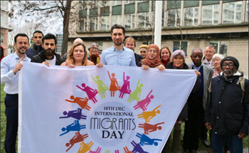 Mayor of Lewisham Damien Egan pictured with a group of people outside Lewisham Council. They hold a banner which reads 'Migrants Day'