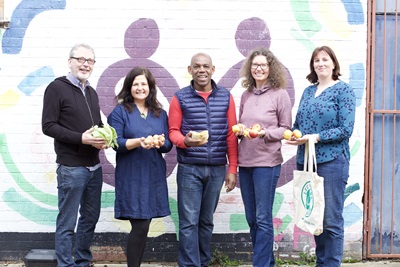 The Lee Greens team standing by a colourful wall holding fresh produce