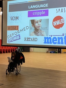 Deptford Green student Millie reading from a piece of paper in front of a screen with words directed as insults to disabled people