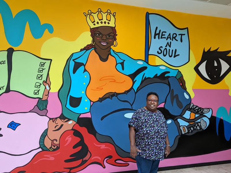 Ono Defedjaiy stands in front of a vibrant painting of herself in Lewisham Shopping Centre