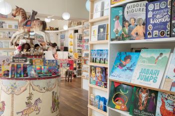 A carousel horse in the middle of the shop with soft toys underneath and lots of colourful books on the shelves