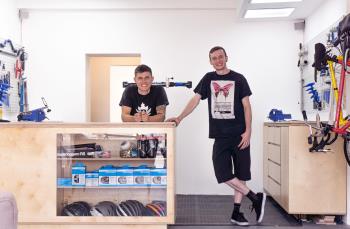 Max and his colleague leaning on the cash register inside The Cyclery surrounded by bikes and cycling accessories