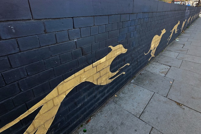 Catford Dogs, Andrew Loakim. Painting of yellow dogs running on Catford Bridge