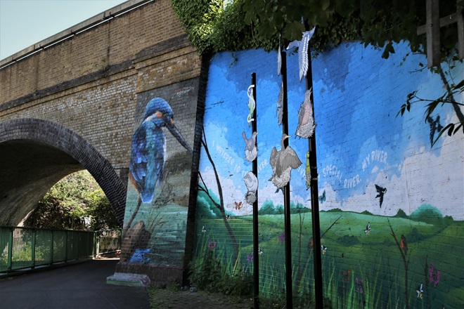 Mural of humming bird next to pole with artwork of birds nesting on city homes