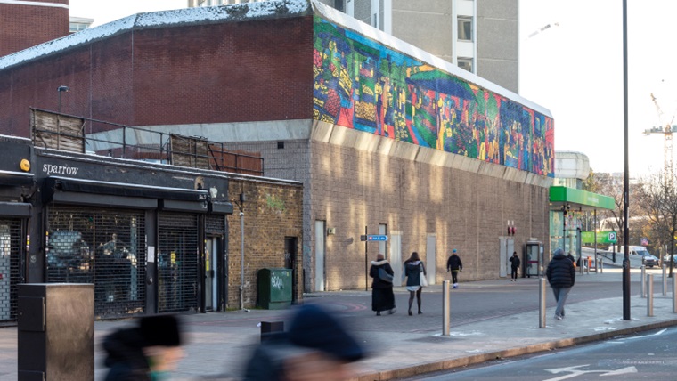 People walking past shopping centre which has a vibrant painting of the market on the buildings side.