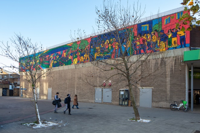 People walking past shopping centre which has a vibrant painting of the market on the buildings side.