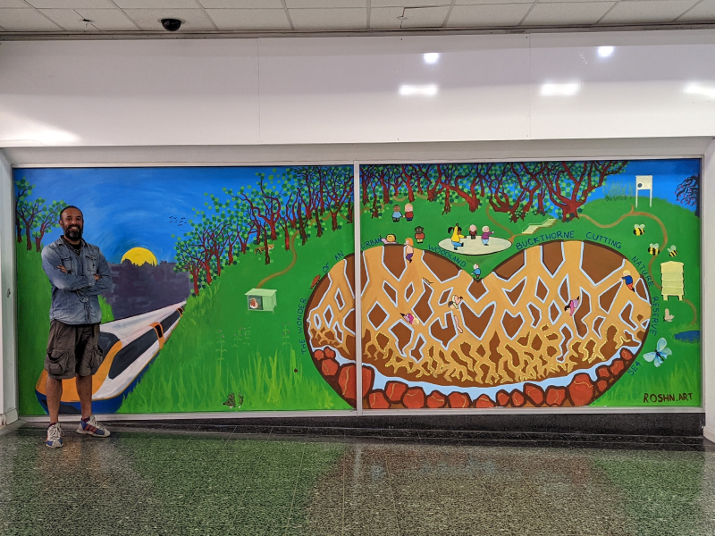 Man, Roshn stands next to mural of Buckthorne Nature Reserve