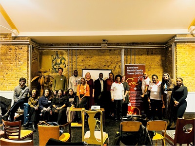 A group of people smile at the camera with a sign behind them that says Lewisham Health Equity Teams