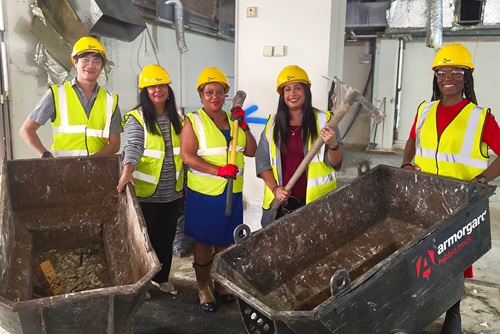 Brenda Dacres and Cllr Sakina Sheikh with staff in construction uniform standing next to wheel boroughs. 