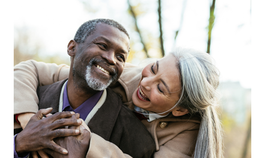 Picture of a couple, likely in their 50s or 60s, embracing outside and smiling.
