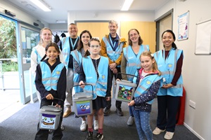 A group of people smile at the camera holding up food waste bins