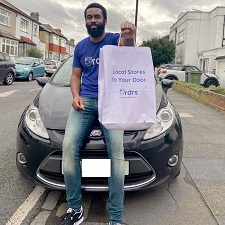 Davidson, a young man is leaning against the bonnet of a car, holding up a white paper bag with the words "Local stores to your door - Ordrs"