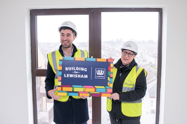 Damien Egan with a representative from Phoenix Community Housing. They are both wearing hard hats and high-vis jackets. They are holding a Building for Lewisham sign.