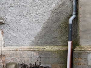 An exterior wall showing render and brickwork water damaged by a leaking gutter