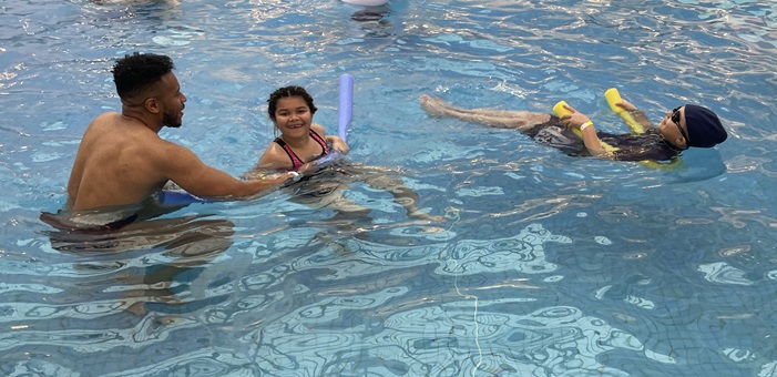 An adult and two children swimming in a swimming pool.